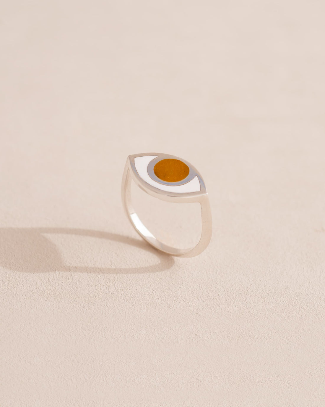 Silver ring with a circular design and orange center on a beige background