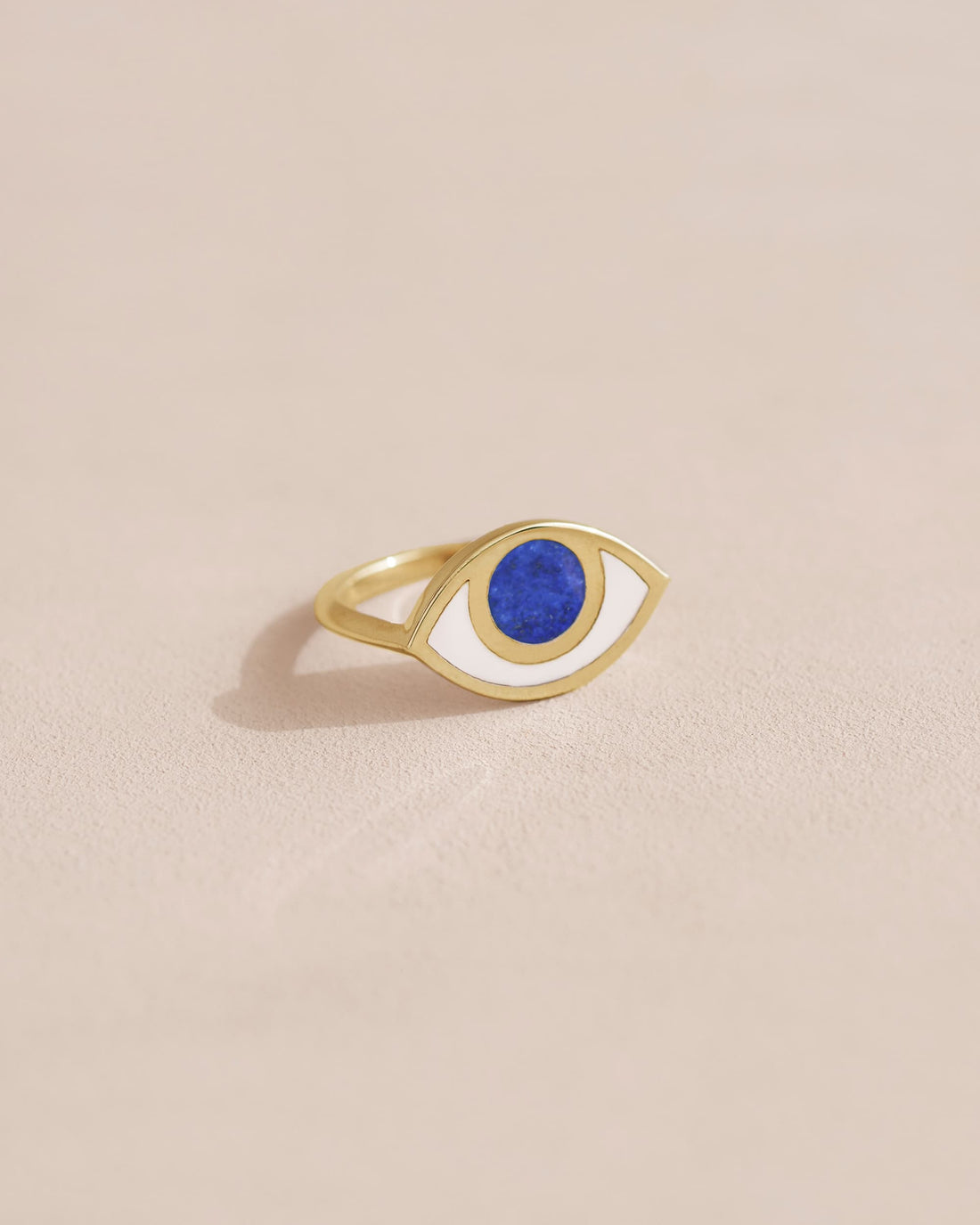 A lapis lazuli ring with a gold band, designed to resemble an eye, placed on a light background.