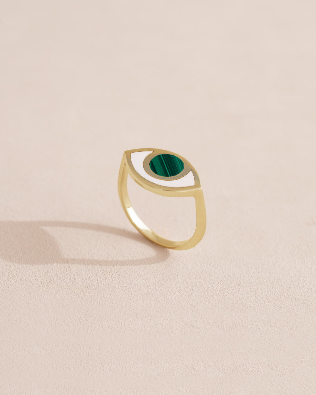 A 14K yellow gold ring with a malachite stone shaped like an eye, placed on a neutral background.