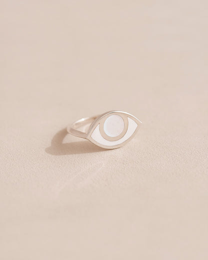A silver-colored ring with a porcelain eye design on a beige background.