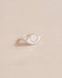 A silver-colored ring with a porcelain eye design on a beige background.