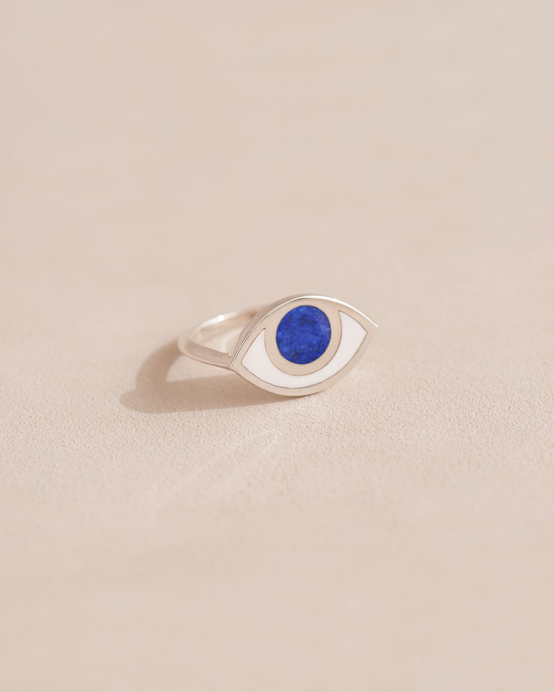 A silver ring shaped like an eye with a lapis lazuli stone set in the center, on a neutral background.