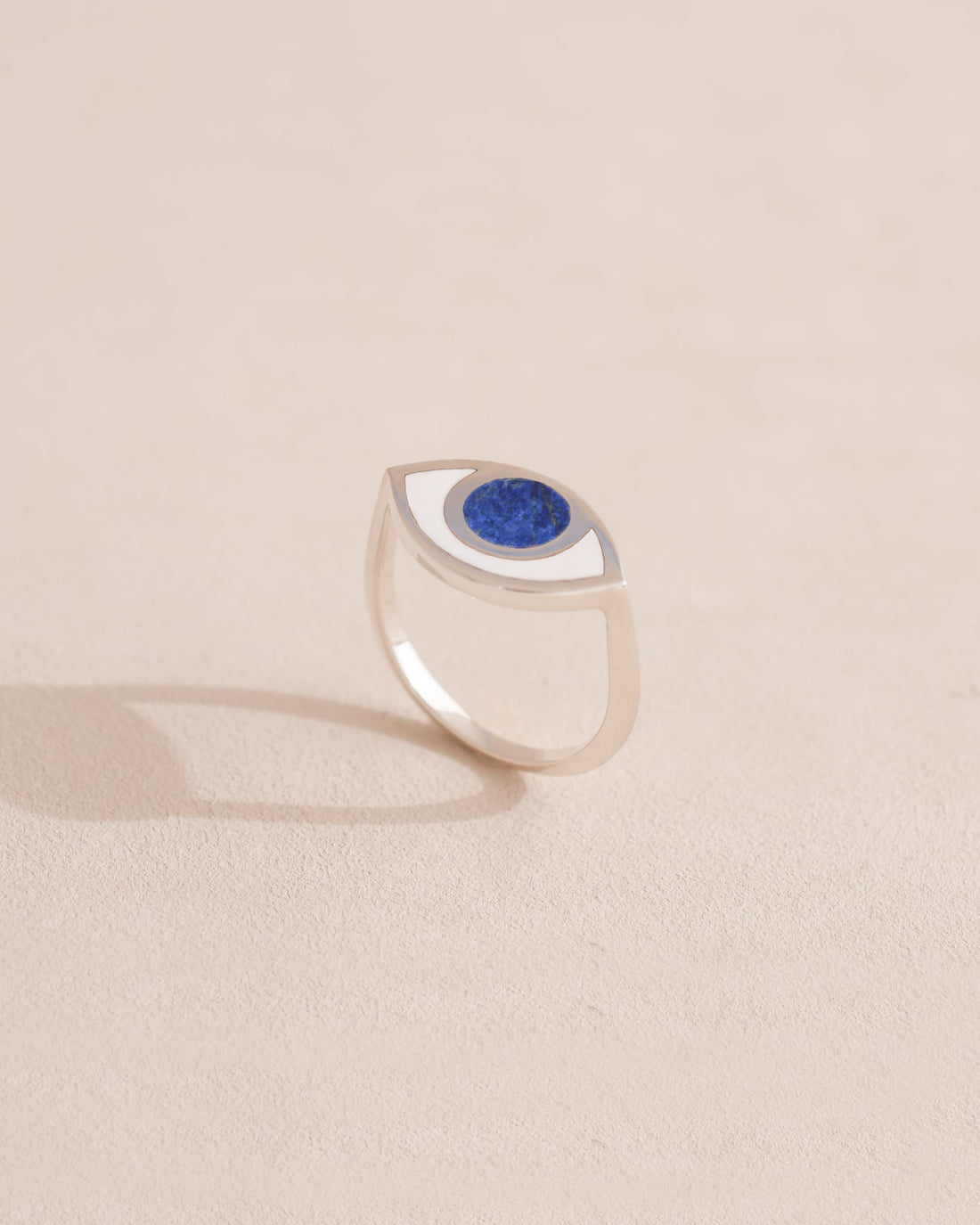 A silver ring shaped like an eye with a lapis lazuli stone set in the center, on a neutral background.