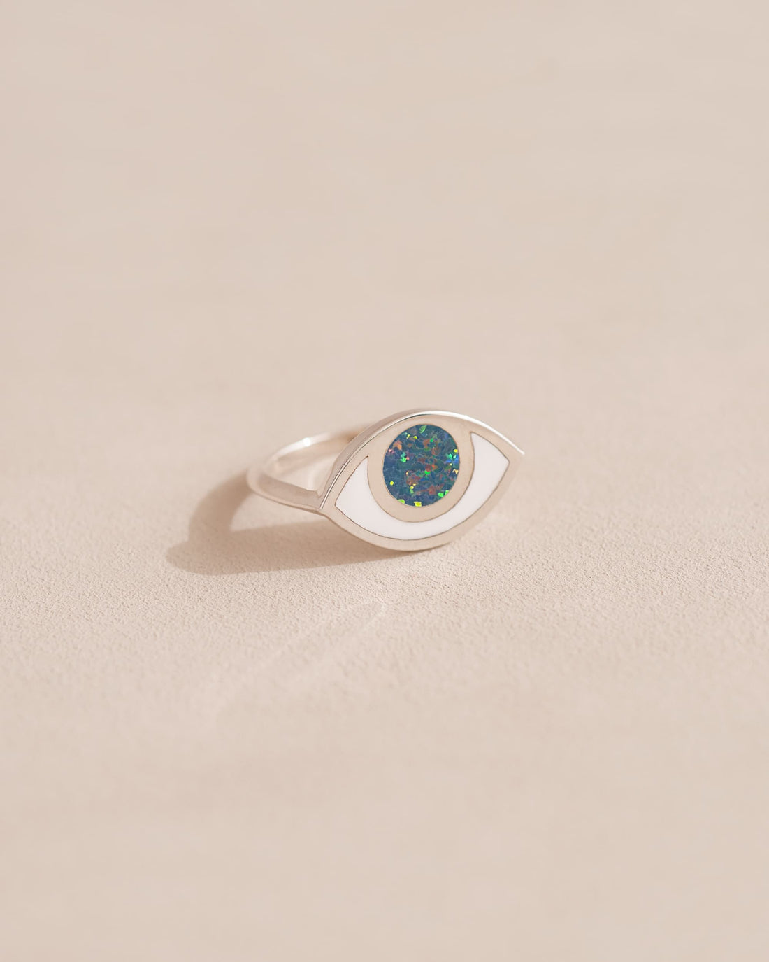 A silver ring shaped like an eye with a dark opal stone set in the center, on a neutral background.