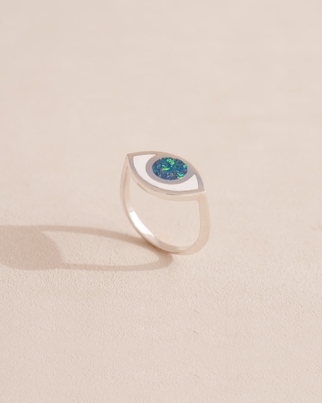 A silver ring shaped like an eye with a starry opal stone set in the center, on a neutral background.