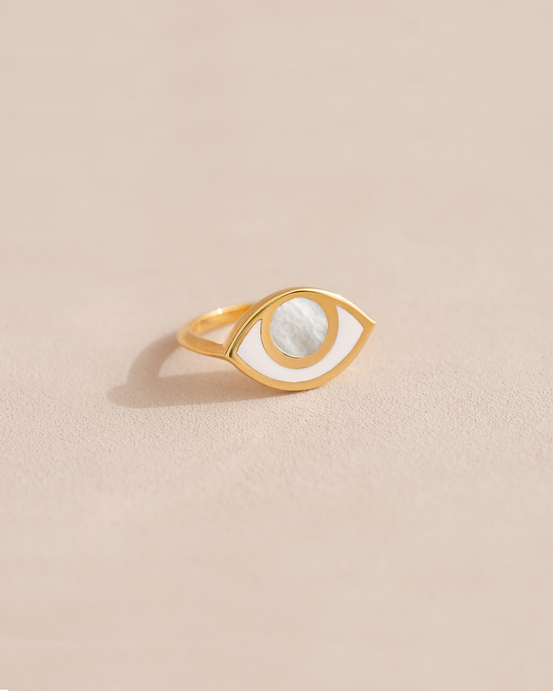 a gold ring shaped like an eye featuring a round mother of pearl center