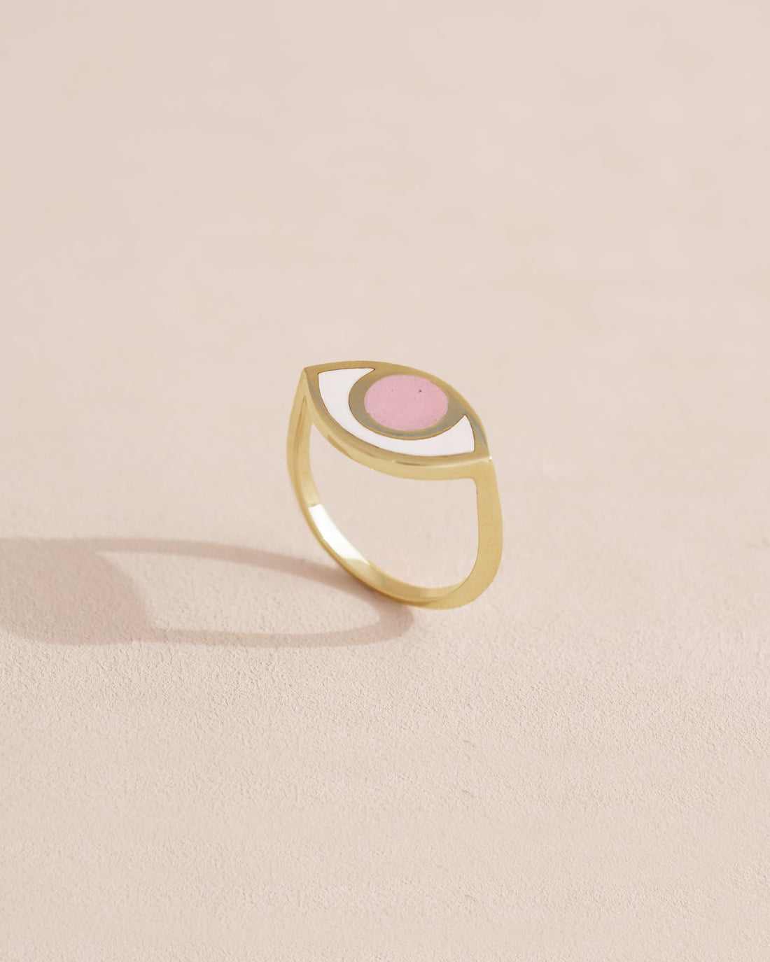 A gold ring with a pink opal centered on the top, placed on a light background.