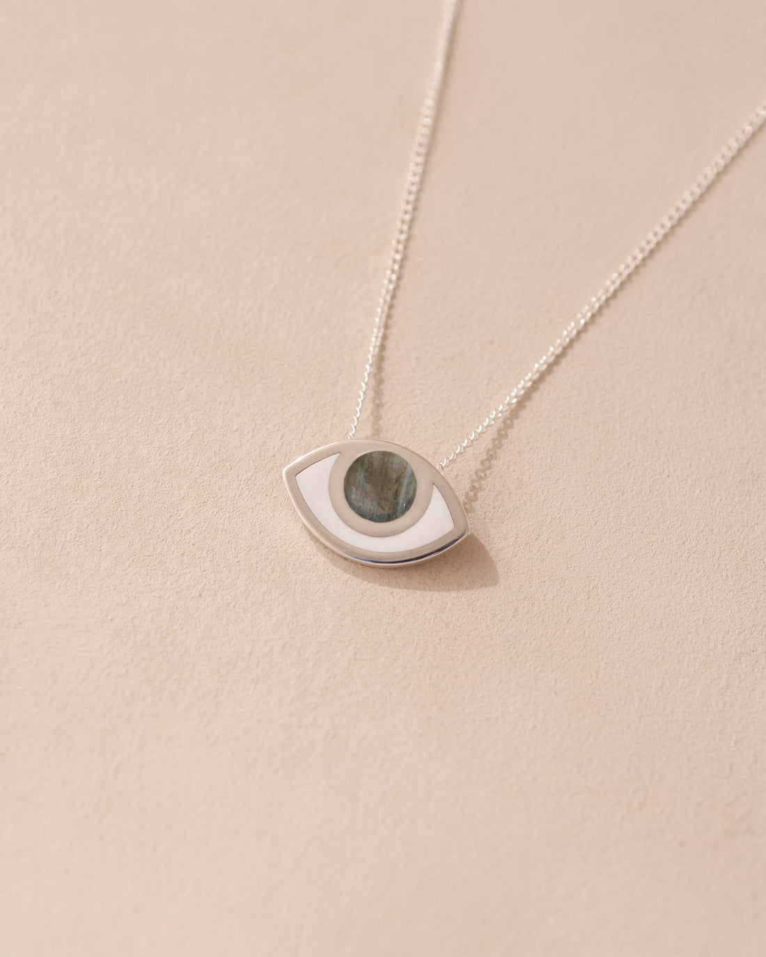 A silver pendant necklace with a labradorite stone in the shape of an eye, displayed against a beige background.