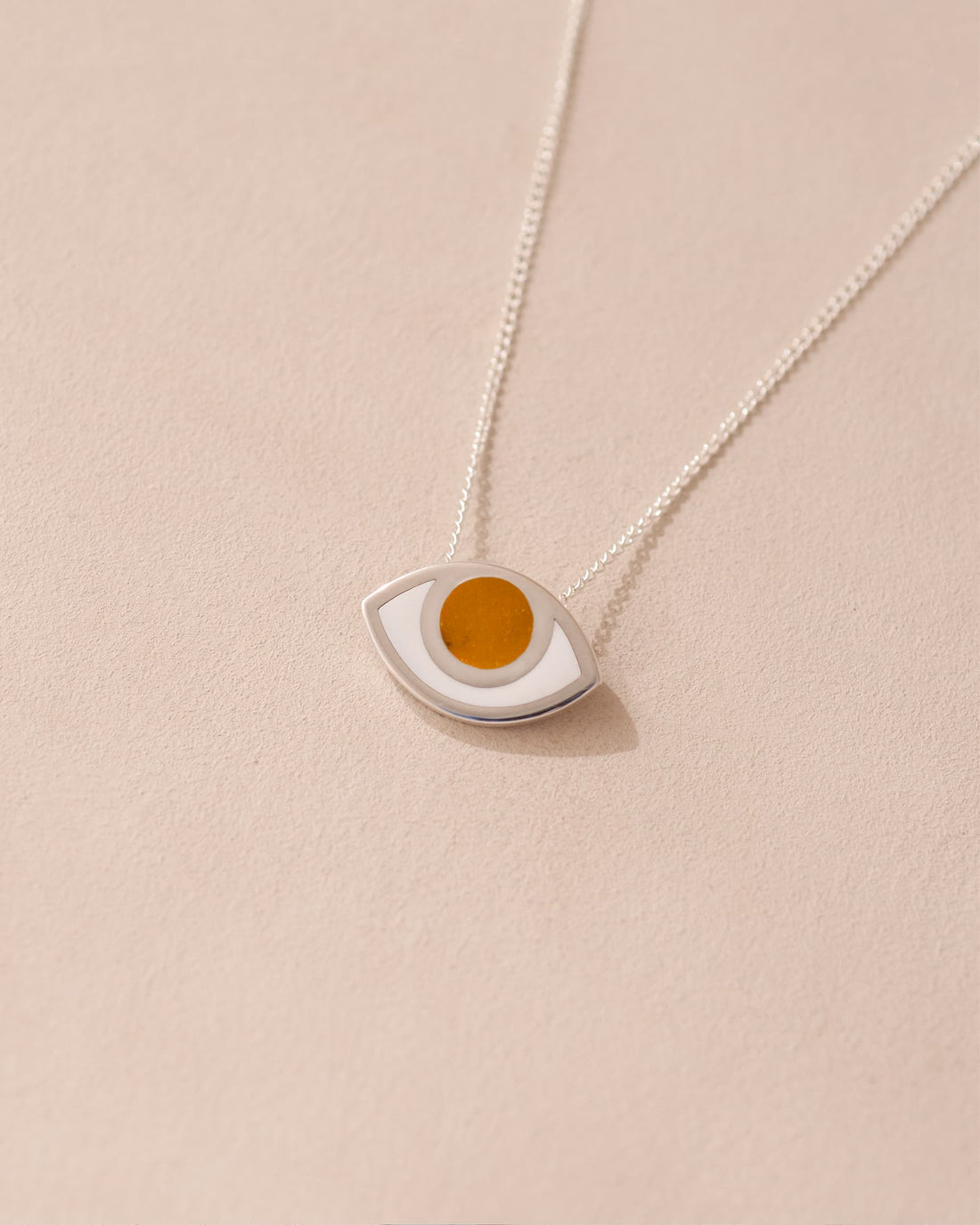 A silver pendant necklace with a round orange mookaite stone set in a eye-shaped frame, displayed against a beige background.