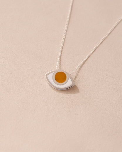A silver pendant necklace with a round orange mookaite stone set in a eye-shaped frame, displayed against a beige background.