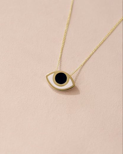 A 14K yellow gold pendant necklace with a black and gold eye design on a beige background.