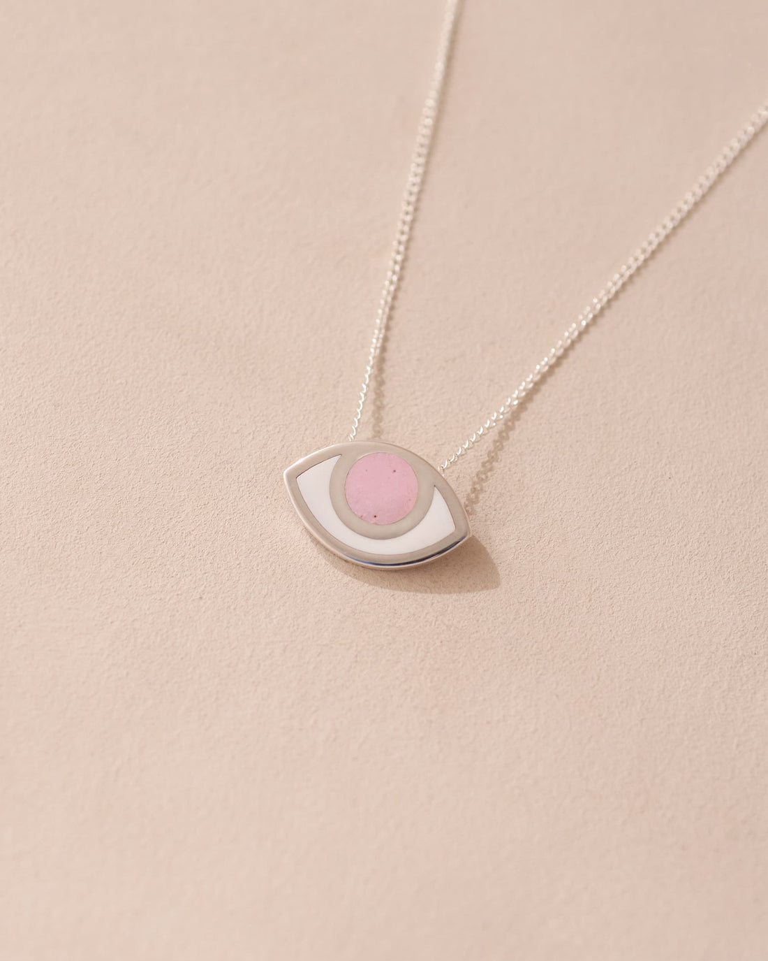 A silver pendant necklace with a pink opal eye design on a beige background.