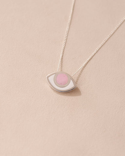 A silver pendant necklace with a pink opal eye design on a beige background.
