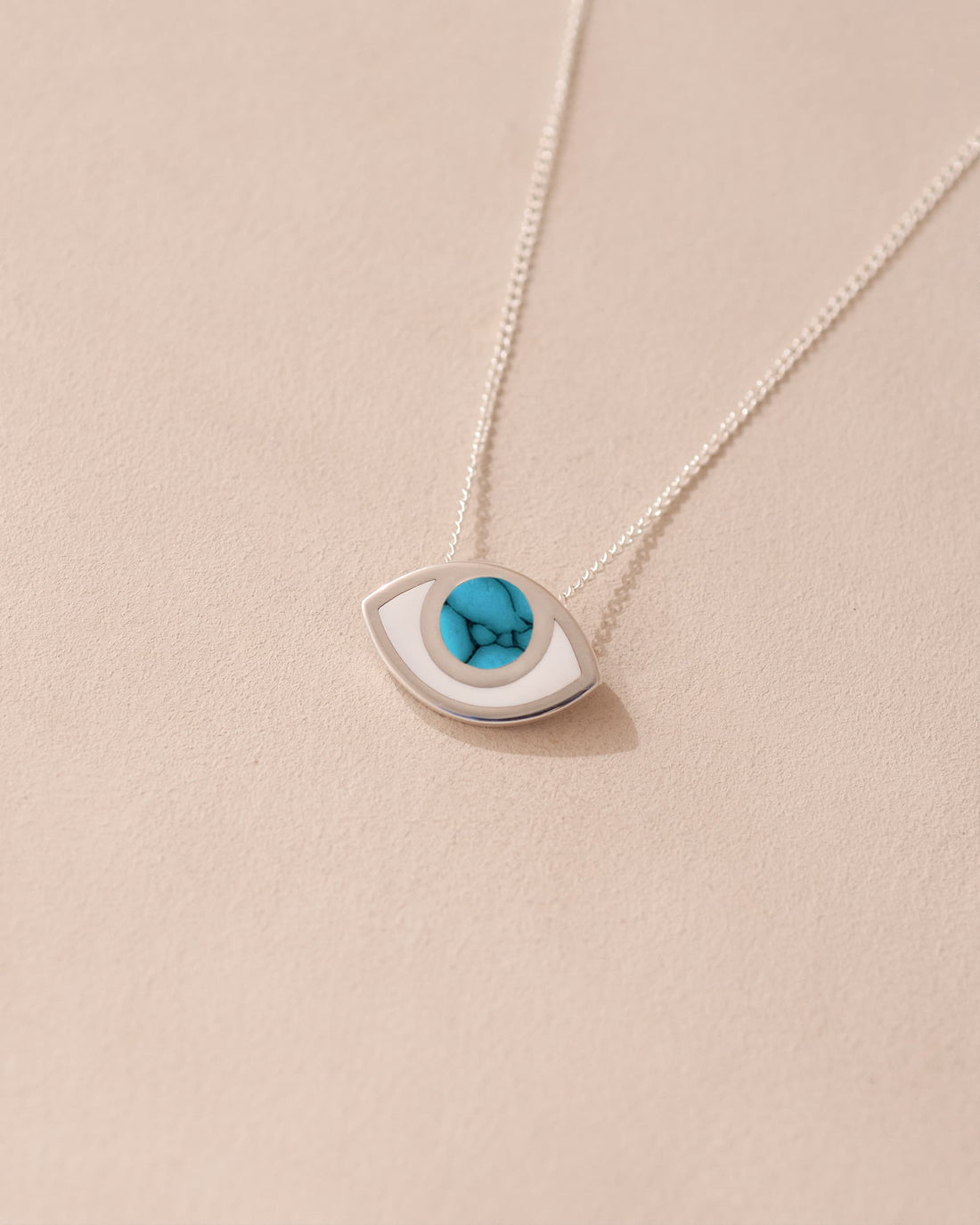 A silver pendant necklace with a turquoise eye-shaped talisman on a light background.
