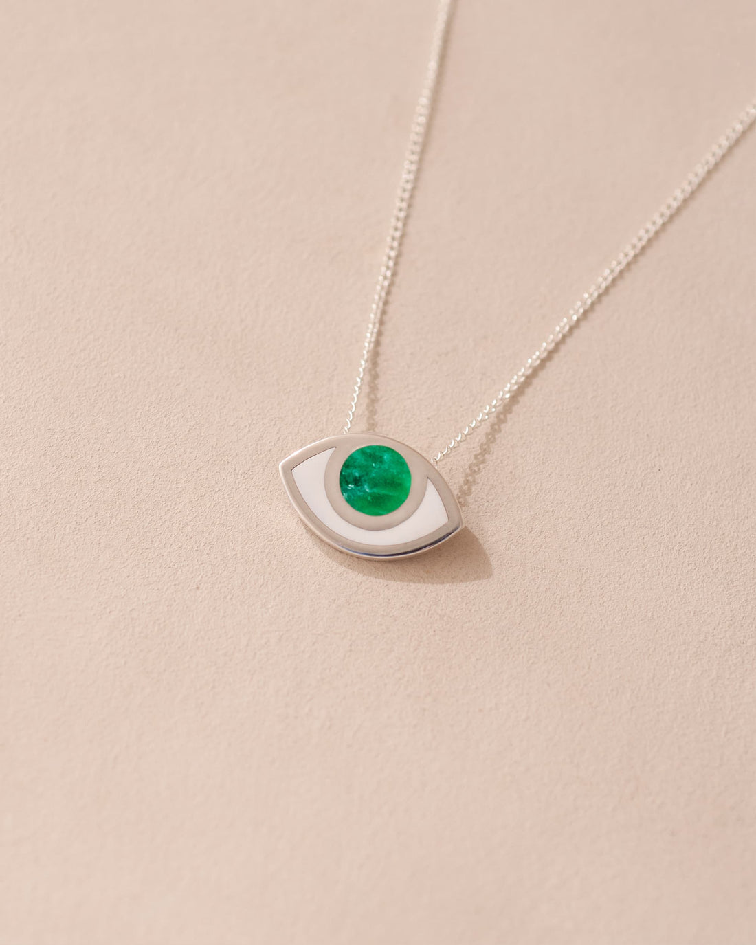 A silver pendant necklace with a variscite stone shaped like an eye, displayed against a beige background.