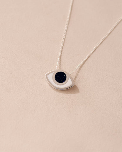 A silver pendant necklace with a goldstone eye design on a beige background.