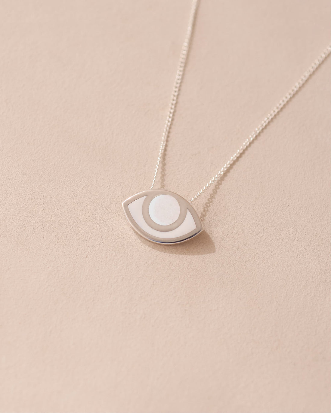 A silver pendant necklace with a porcelain eye design, displayed against a beige background.