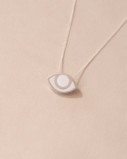 A silver pendant necklace with a porcelain eye design, displayed against a beige background.