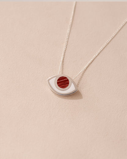 A silver pendant necklace with a round red snakeskin jasper stone in the shape of an eye, displayed against a beige background.