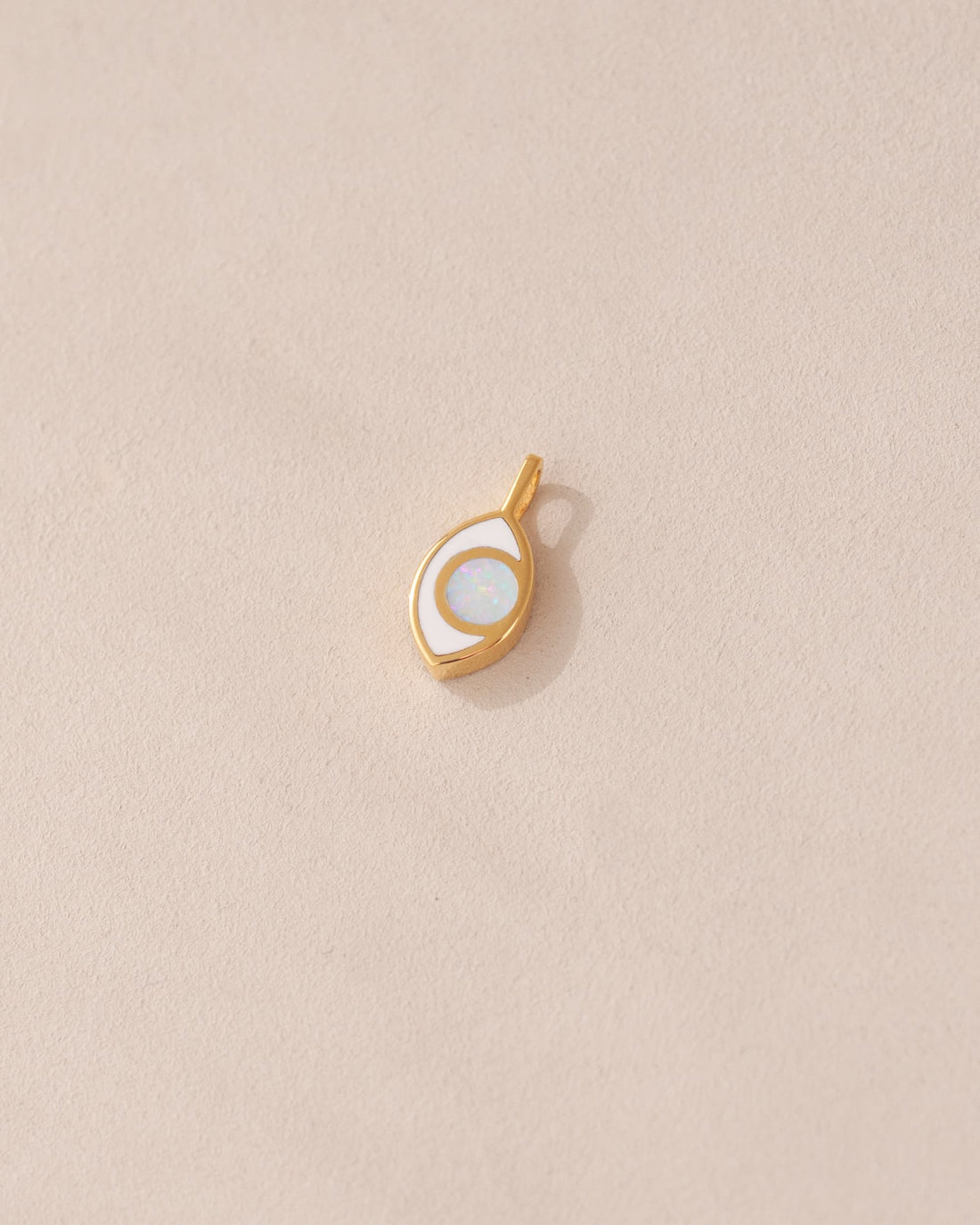 a gold charm shaped like an eye featuring a round opal center