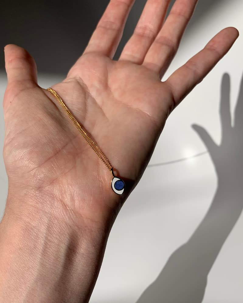 A hand holding a gold eye shaped charm hanging from a gold chain