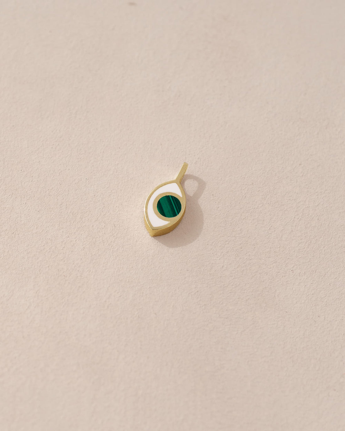A small 14K yellow gold charm with a malachite stone shaped like an eye, placed on a light background.