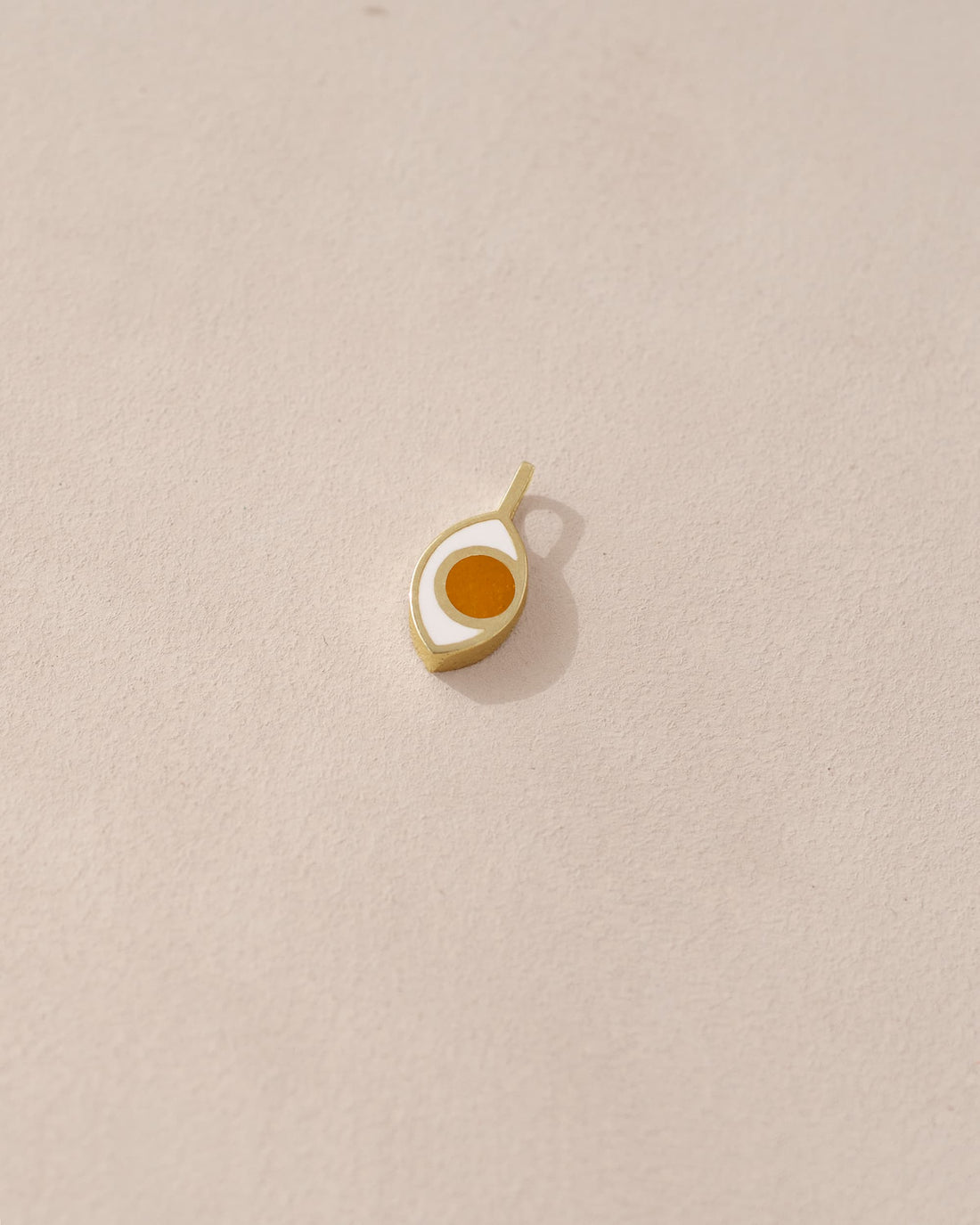 A small gold-colored charm in the shape of an eye on a light background.