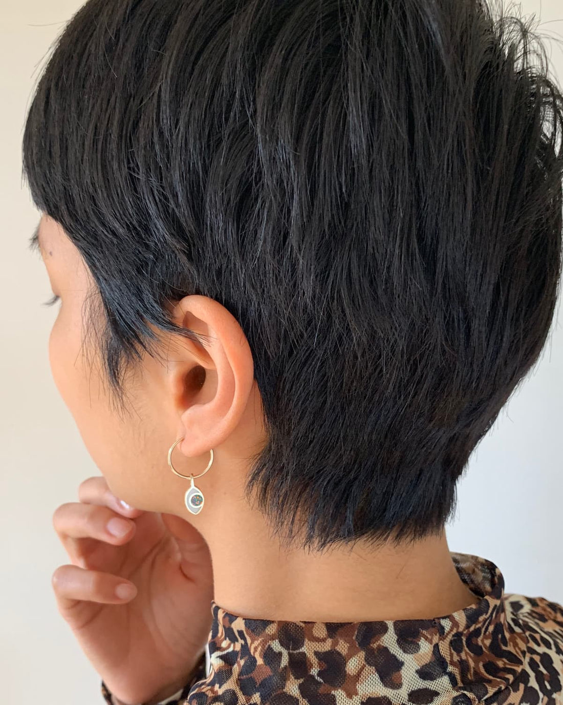 a short haired model wearing an eye shaped charm hanging from a hoop on her ear