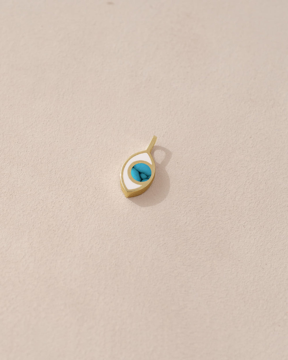 A small turquoise charm in the shape of an eye set in a gold frame, displayed against a beige background.