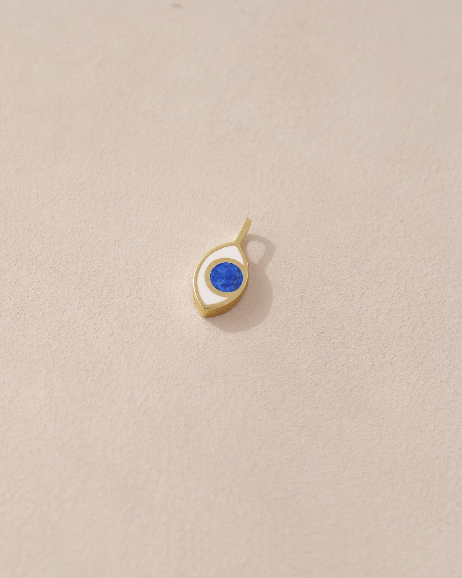 A small lapis lazuli charm in a gold setting, shaped like an eye, placed against a beige background.