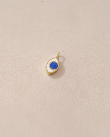 A small lapis lazuli charm in a gold setting, shaped like an eye, placed against a beige background.