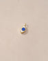 A small lapis lazuli charm in a gold setting, shaped like an eye, placed against a beige background.