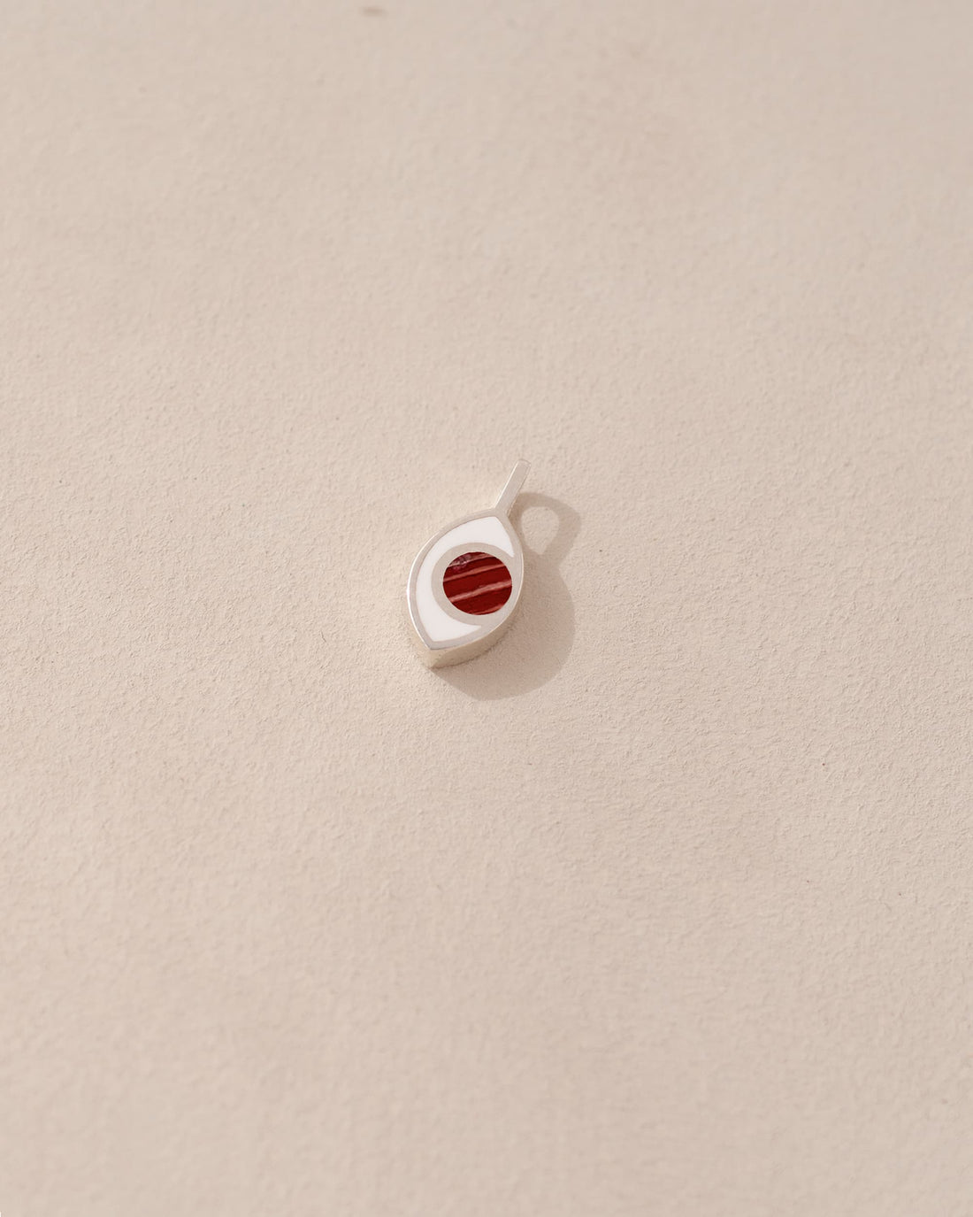 A small silver charm with a jasper stone in the shape of an eye, placed on a light background.