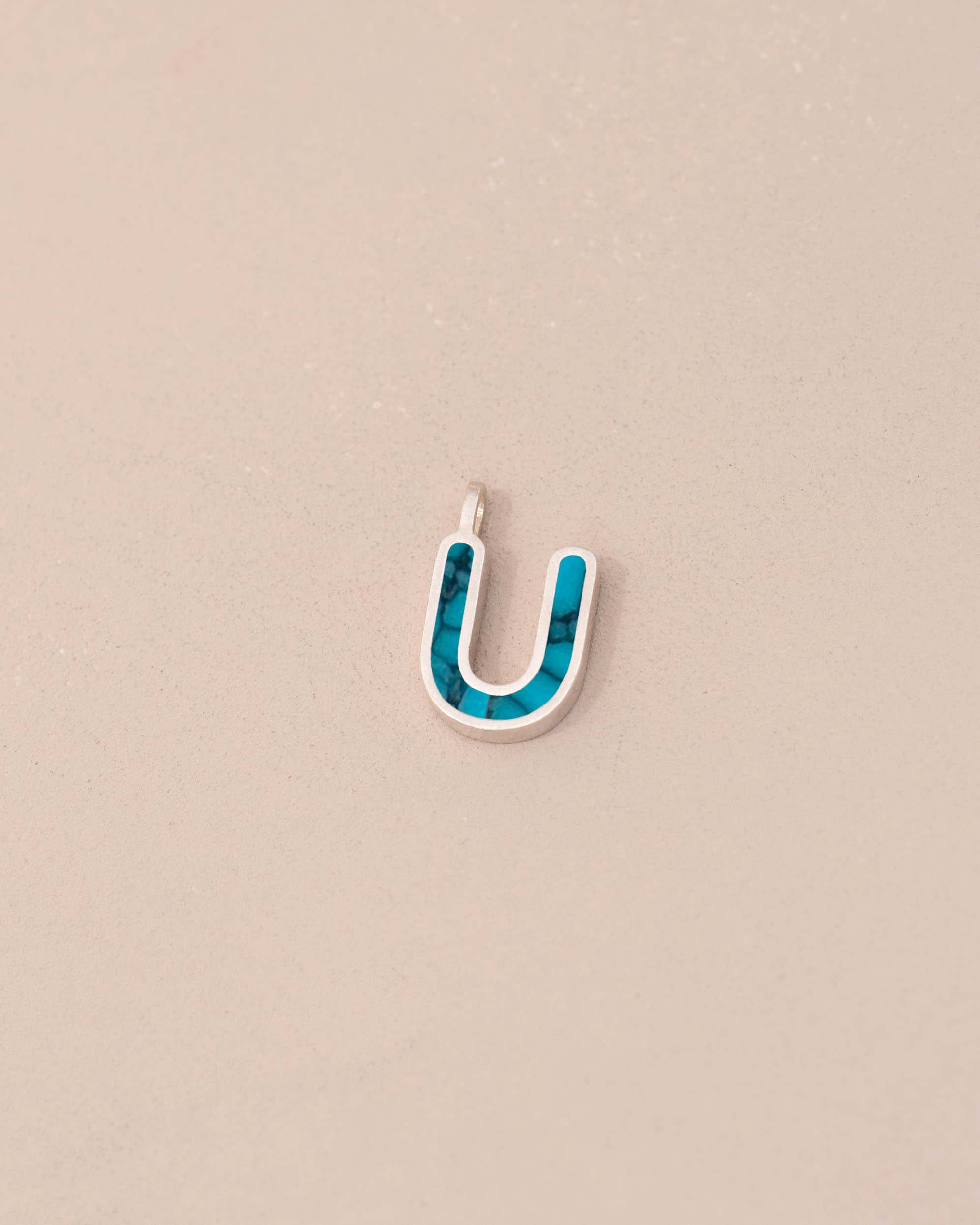 Blue and silver U-shaped pendant on a beige background