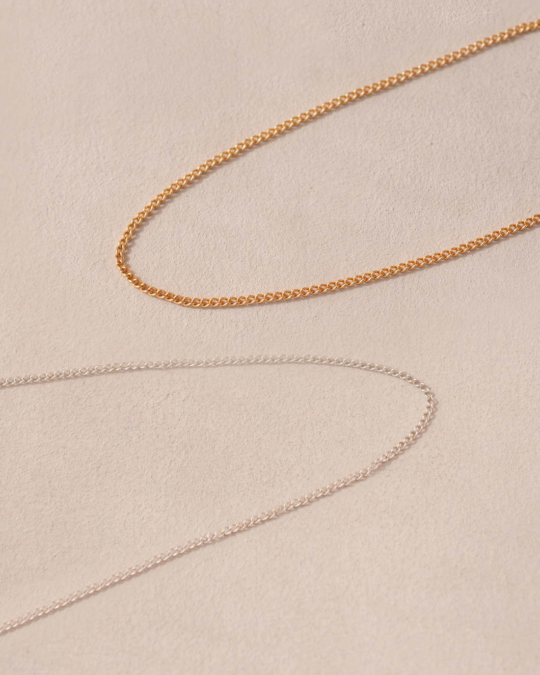 A close-up image of a 14K yellow gold curved chain necklace laid out on a textured background.