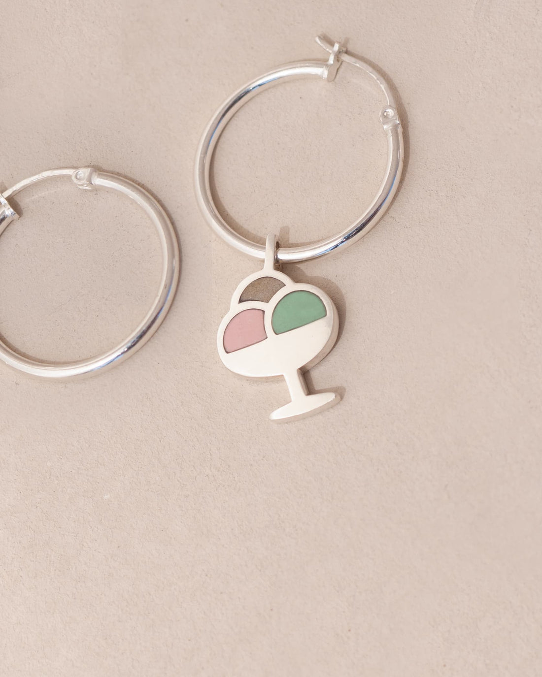 Silver hoop earrings with a heart and ice cream cone charm on a beige background