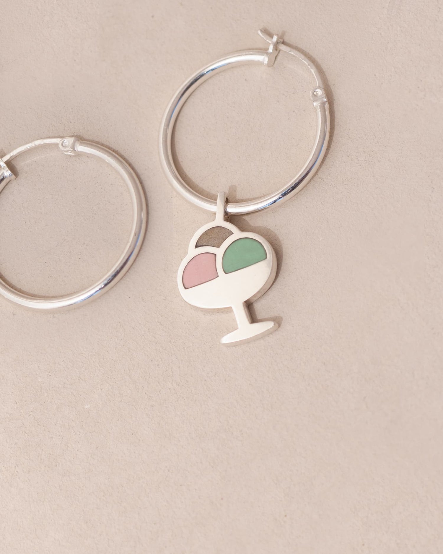 Silver hoop earrings with a heart and ice cream cone charm on a beige background