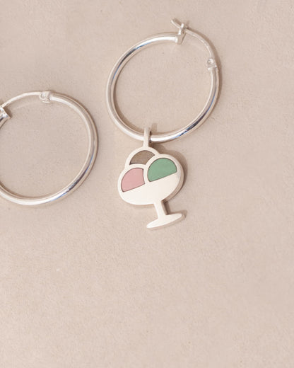 Silver hoop earrings with a heart and ice cream cone charm on a beige background