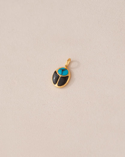 A 14K yellow gold charm in the shape of a scarab amulet with turquoise and onyx inlays, displayed against a neutral background.